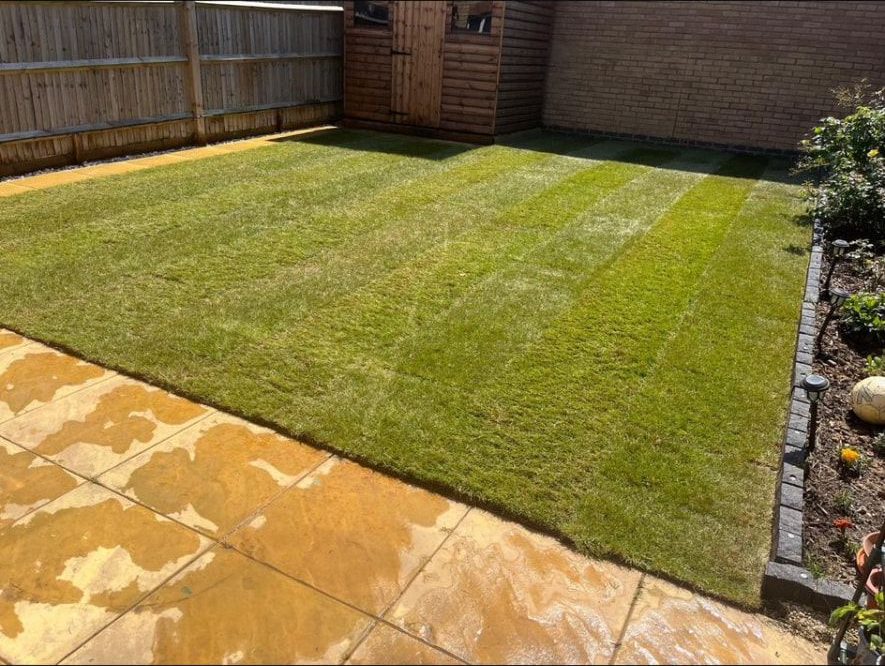 Newly laid turf beside sandstone paving and a timber shed